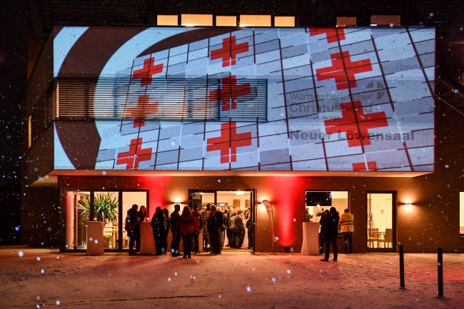 zu sehen ist eine Lichtpräsentation eines DRK-Logos auf die Eingangswand des Löwensaals Weilheim