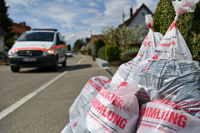 Altkleidersammlung zu sehen ist ein DRK-Fahrzeug auf der Straße und ein Haufen mit Altkleidersäcken am Straßenrand bei einer Sammlung