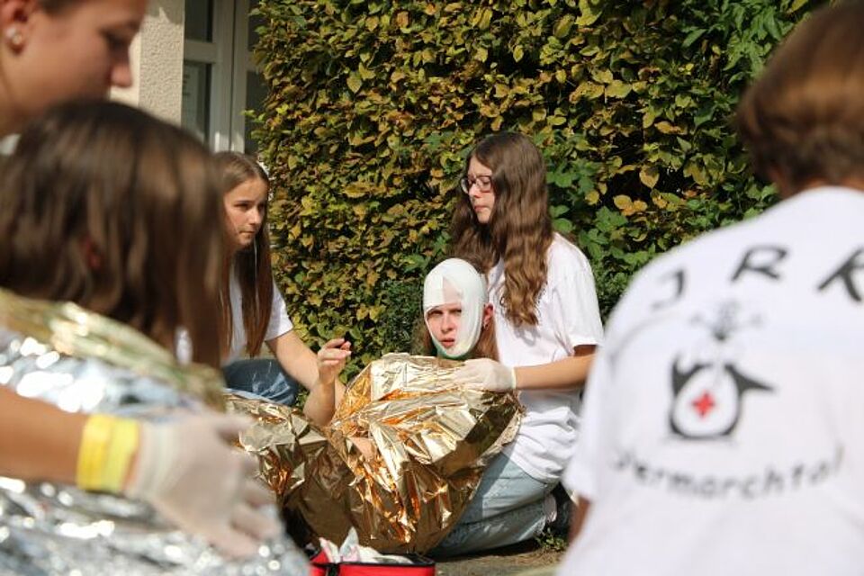 zu sehen ist eine Mime, welche durch DRK-Helfer*innen am Internationalen Wettbewerb mit Erste Hilfe versorgt wird