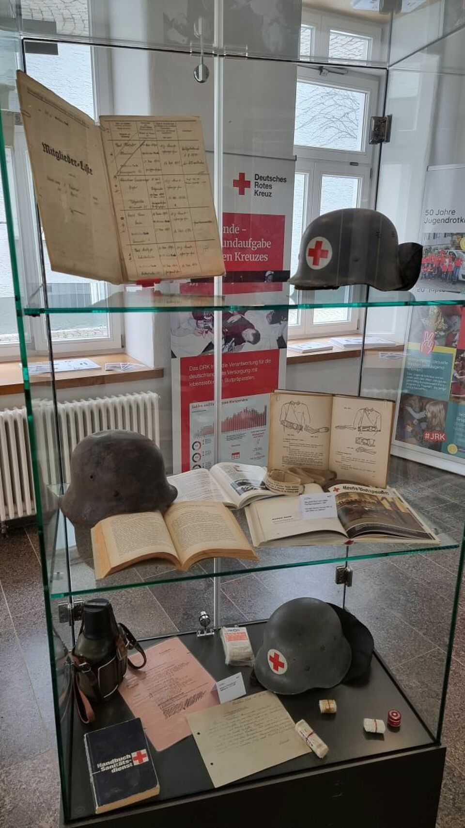 zu sehen ist eine Vitrine in der Ausstellung mit älteren Schriftstücken und Kopfbedeckungen
