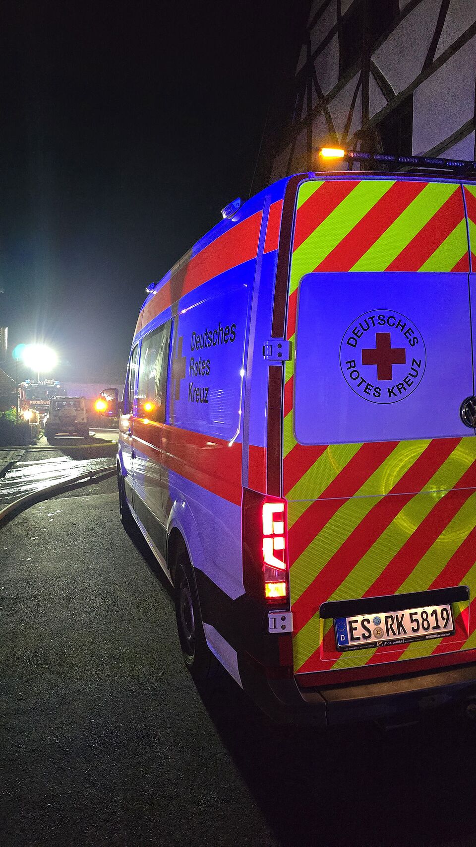 zu sehen ist ein DRK-Fahrzeug und im Hintergrund das betroffene Brandgebäude